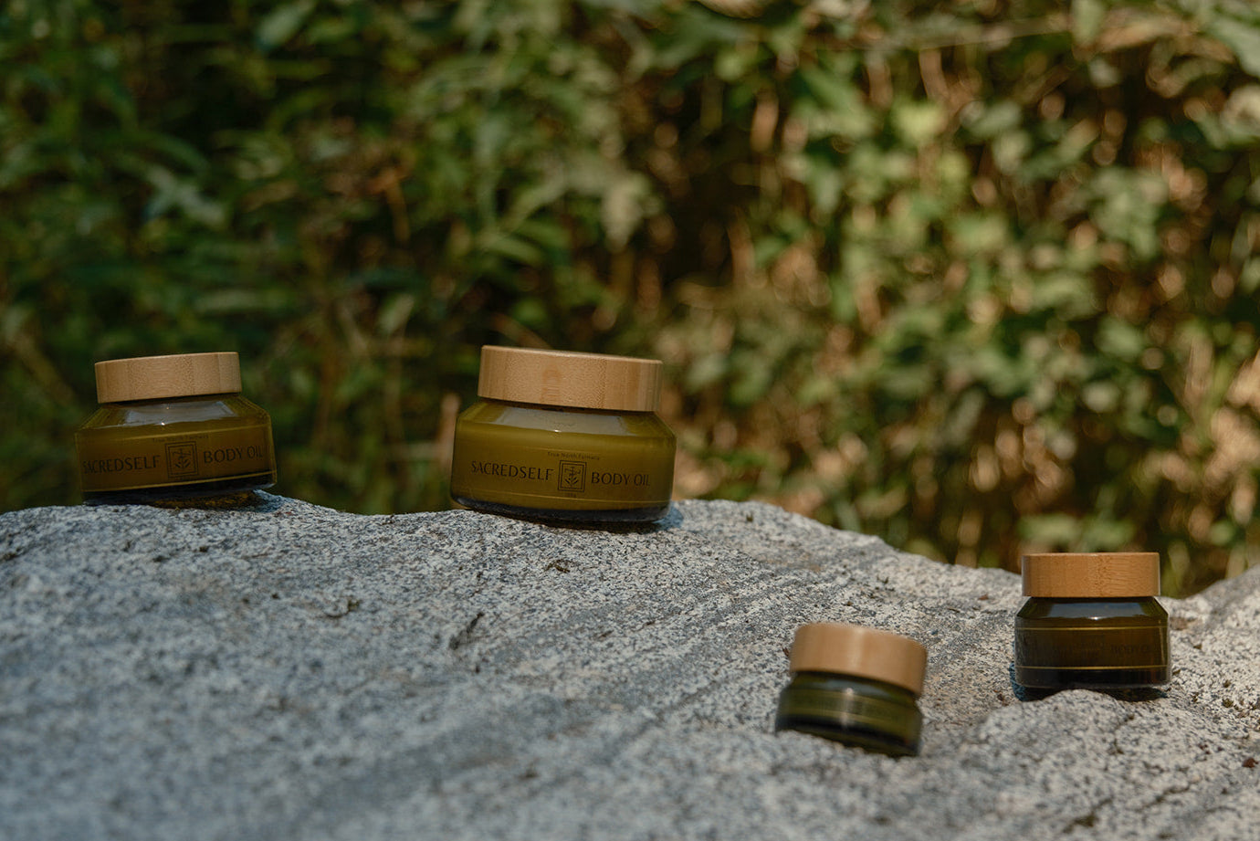 Small Batch Body Oil various sized jars with bamboo lids on a stone surface in nature